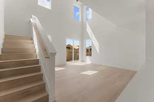 Unfurnished living room with plenty of natural light, wood finished floors, stairs, a towering ceiling, and baseboards