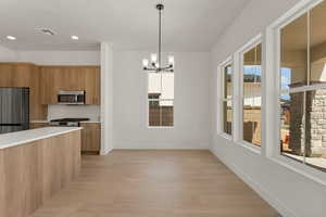 Kitchen featuring stainless steel appliances, brown cabinetry, a chandelier, light countertops, and light wood finished floors