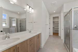 Full bathroom featuring a stall shower, a spacious closet, double vanity, baseboards, and recessed lighting