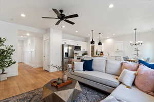 Living room featuring light wood-style floors, a ceiling fan, recessed lighting, a chandelier, and baseboards