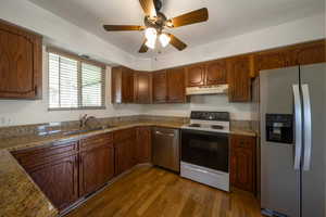 Kitchen featuring stainless steel appliances, under cabinet range hood, a sink, dark wood-style floors, and a ceiling fan