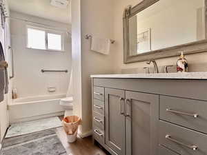Full bath featuring toilet, vanity, wood finished floors, shower / tub combo, and baseboards