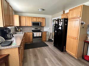 Kitchen featuring stainless steel appliances, a sink, backsplash, wood finished floors, and light countertops