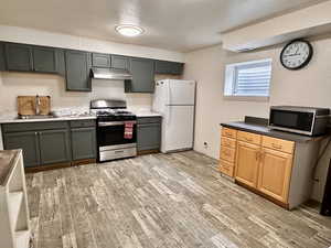 Kitchen with stainless steel appliances, under cabinet range hood, a sink, light wood-type flooring, and baseboards