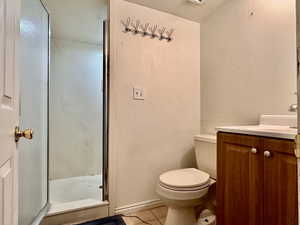 Bathroom featuring tile patterned floors, a textured wall, toilet, a stall shower, and vanity