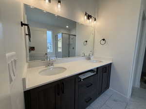 Bathroom featuring a shower stall, double vanity, marble finish flooring, and baseboards