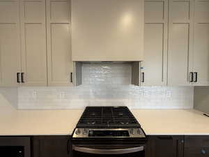 Kitchen with stainless steel gas range oven, light countertops, decorative backsplash, and custom range hood