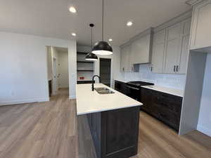 Kitchen featuring a sink, light countertops, light wood-style floors, black gas stove, and recessed lighting