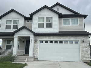 Craftsman-style home with stone siding, driveway, an attached garage, and covered porch