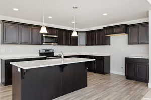 Kitchen with stainless steel appliances, light wood-style flooring, pendant lighting, an island with sink, and a kitchen breakfast bar