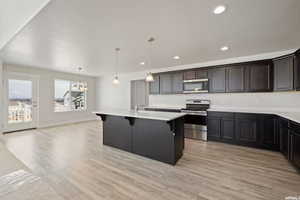 Kitchen featuring stainless steel appliances, a kitchen bar, light countertops, light wood-style flooring, and recessed lighting