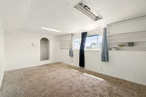 Carpeted spare room with a textured ceiling, baseboards, and vaulted ceiling