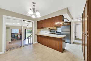 Kitchen with appliances with stainless steel finishes, light countertops, a peninsula, decorative backsplash, and a chandelier