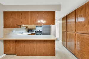 Kitchen featuring stainless steel appliances, a peninsula, light countertops, a sink, and brown cabinetry