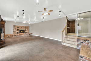 Unfurnished living room with ceiling fan, finished concrete floors, stairs, a brick fireplace, and baseboards