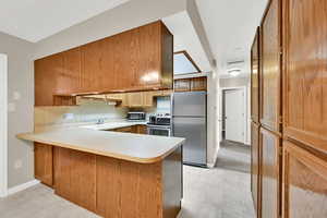 Kitchen with stainless steel appliances, light countertops, decorative backsplash, a peninsula, and a sink