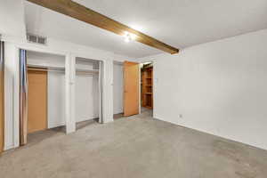 Unfurnished bedroom with concrete flooring, beamed ceiling, and two closets