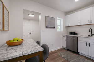 Kitchen featuring stainless steel dishwasher, a sink, dark wood-style floors, white cabinets, and recessed lighting
