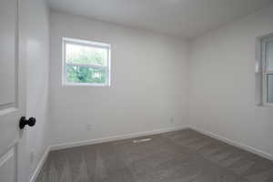 Spare room featuring dark colored carpet and baseboards