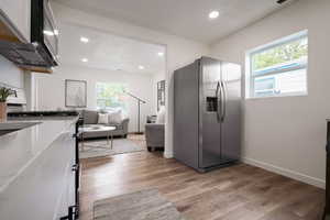 Kitchen with stainless steel fridge with ice dispenser, recessed lighting, light wood-style floors, baseboards, and light stone counters