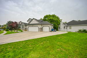 View of front of property featuring an attached garage, concrete driveway, a front lawn, stone siding, and stucco siding