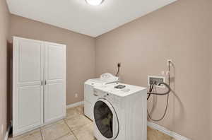Clothes washing area with washer / clothes dryer, cabinet space, baseboards, and light tile patterned floors