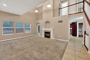 Unfurnished living room featuring baseboards, a high ceiling, tile patterned flooring, a tile fireplace, and carpet floors