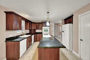 Kitchen with white appliances, a sink, dark countertops, a center island, and light tile patterned floors