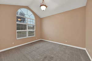 Carpeted spare room featuring vaulted ceiling and baseboards