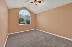 Unfurnished room featuring ceiling fan, lofted ceiling, carpet floors, and baseboards