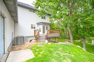 Rear view of property with stucco siding, a deck, central AC, and a yard