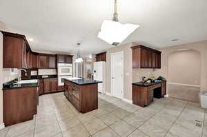 Kitchen with white appliances, a sink, arched walkways, dark countertops, and recessed lighting
