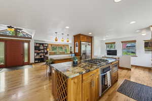 Kitchen with appliances with stainless steel finishes, a kitchen island, brown cabinetry, light wood-style floors, and recessed lighting