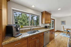Kitchen with dishwasher, a sink, brown cabinets, light wood-type flooring, and light stone counters