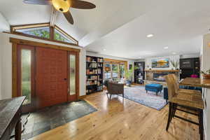 Entryway featuring a stone fireplace, ceiling fan, vaulted ceiling, recessed lighting, and wood finished floors