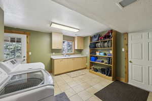 Laundry area featuring washing machine and clothes dryer, cabinet space, a textured ceiling, baseboards, and light tile patterned floors
