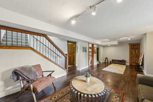 Living room with rail lighting, stairs, wood finished floors, and baseboards