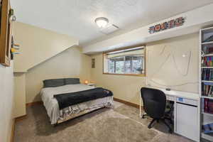 Bedroom with light carpet, baseboards, a textured ceiling, and an office area