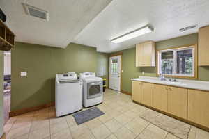 Laundry area with a textured ceiling, baseboards, washer and clothes dryer, cabinet space, and light tile patterned floors