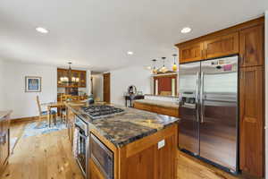 Kitchen featuring appliances with stainless steel finishes, brown cabinets, a chandelier, a kitchen island, and recessed lighting