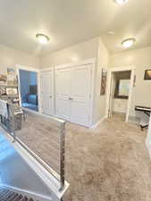 Corridor with a textured ceiling, baseboards, and light colored carpet