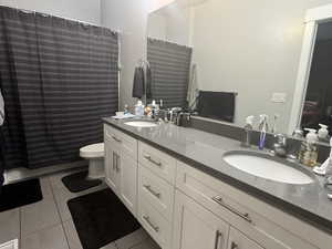Full bath with tile patterned flooring, toilet, double vanity, and curtained shower