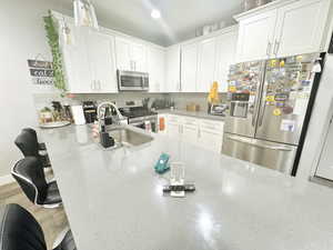 Kitchen featuring appliances with stainless steel finishes, a breakfast bar, a sink, white cabinetry, and hanging light fixtures