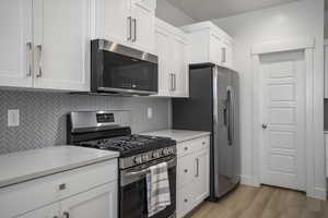 Kitchen with stainless steel appliances, decorative backsplash, light countertops, light wood-style floors, and white cabinetry