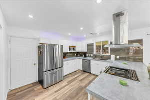 Kitchen featuring stainless steel appliances, ventilation hood, a sink, light wood-style floors, and decorative backsplash