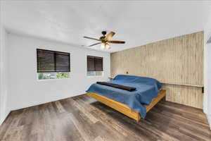 Bedroom featuring wood finished floors, wood walls, a ceiling fan, and baseboards