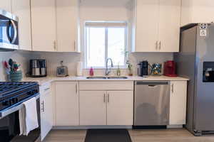 Kitchen with appliances with stainless steel finishes, a sink, light countertops, white cabinetry, and light wood-style flooring