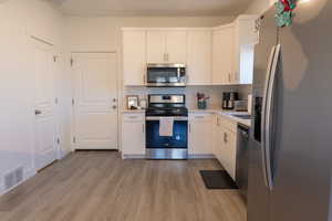 Kitchen with stainless steel appliances, light wood-type flooring, light countertops, and white cabinets