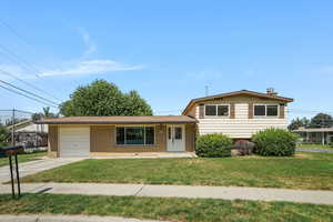 Split level home with a garage, concrete driveway, a front yard, and brick siding