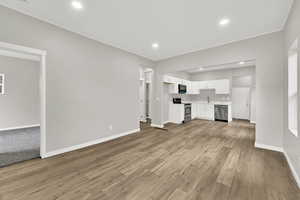 Unfurnished living room with baseboards, ornamental molding, light wood finished floors, recessed lighting, and a sink